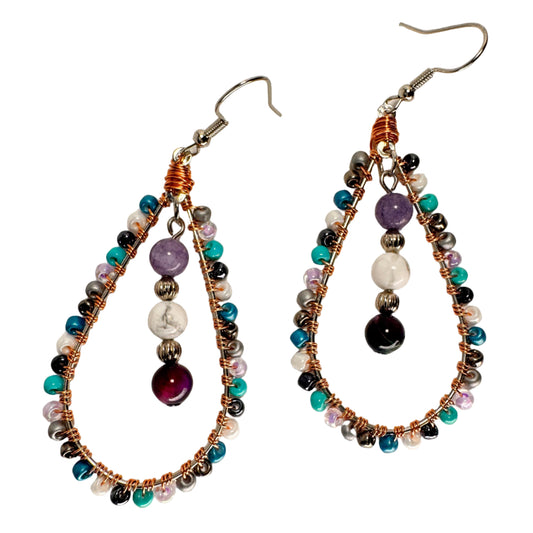 Close-up detail of copper and pastel colored seed beads wrapped around a teardrop-shaped frame with amethyst, howlite, and galaxy tiger's eye dangling in the middle of the Celestial Tears earrings showing artisan craftmanship
