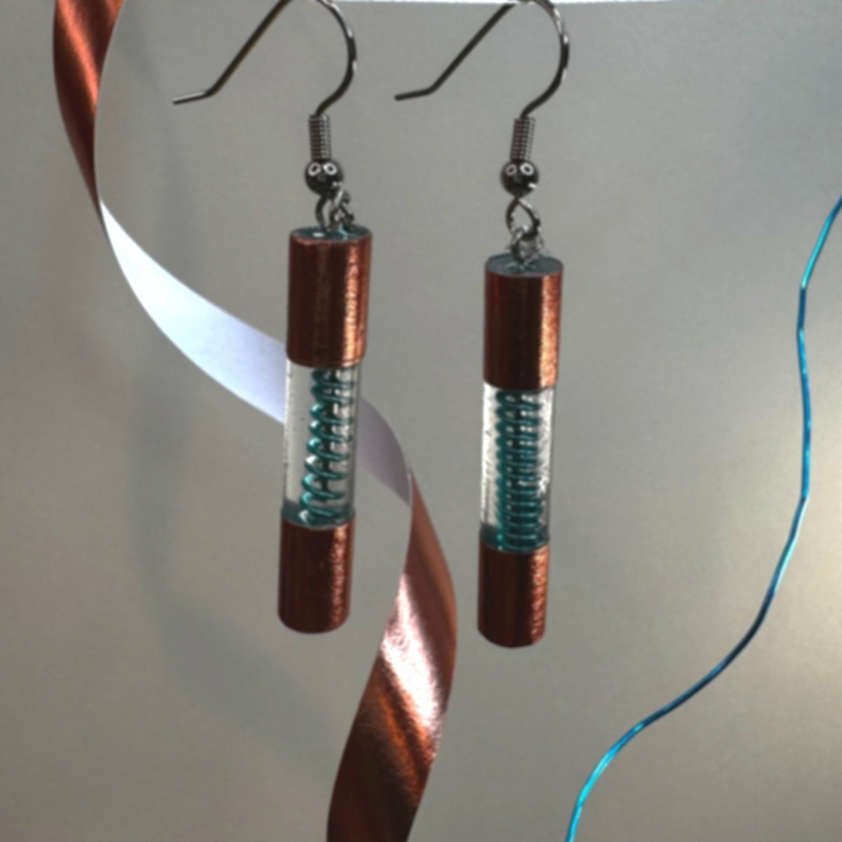 Clear resin form a cylinder encasing a blue spiral wire. Outside of the cylinder is wrapped on both ends in copper washi tape to make the dangle look like a fuse.