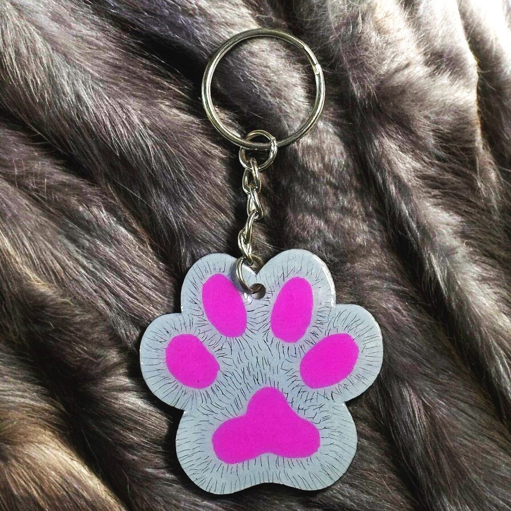 paw shaped keychain with gray background that has been scratched to give the effect of fur. 