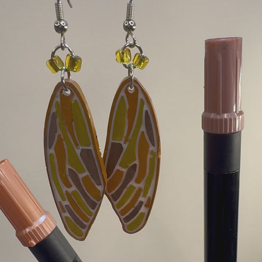 Resin formed earrings colored in copper, gold, and metallic brown resemble the wings of a cicada