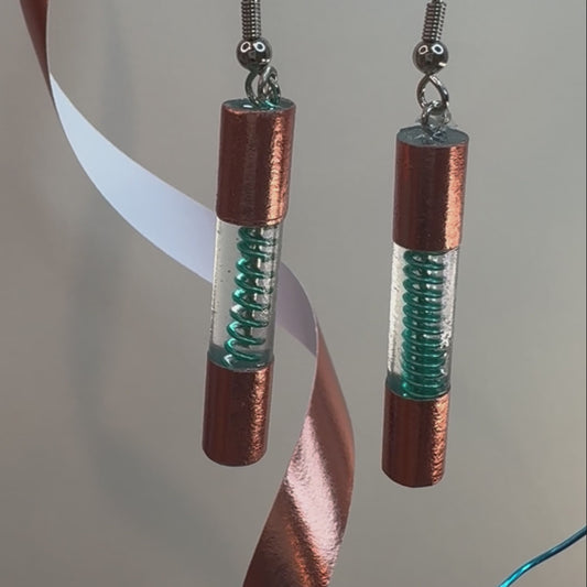 Clear resin form a cylinder encasing a blue spiral wire. Outside of the cylinder is wrapped on both ends in copper washi tape to make the dangle look like a fuse.