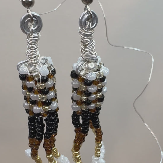 Brown, Black, White, and Gold beads woven together form a cylinder and have stacks of beads hanging down, making a chandelier style earring.