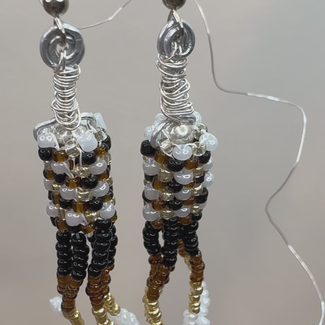 Brown, Black, White, and Gold beads woven together form a cylinder and have stacks of beads hanging down, making a chandelier style earring.