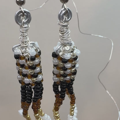 Brown, Black, White, and Gold beads woven together form a cylinder and have stacks of beads hanging down, making a chandelier style earring.